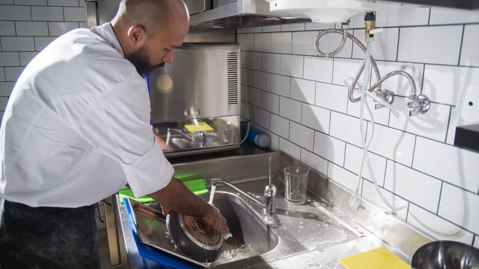 A chef scrubbing a pan in a stainless steel sink, one of the daily tasks on a restaurant cleaning schedule